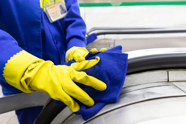 Fotografía de una persona que trabaja como auxiliar de limpieza utilizando guantes amarillos para limpiar una banda.