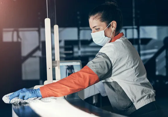 Fotografía de una mujer que trabaja como auxiliar de limpieza industrial utilizando guantes y cubrebocas.