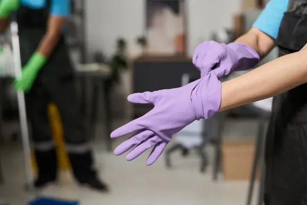 Fotografía de una persona que es auxiliar de limpieza industrial colocándose guantes color morado antes de trabajar.