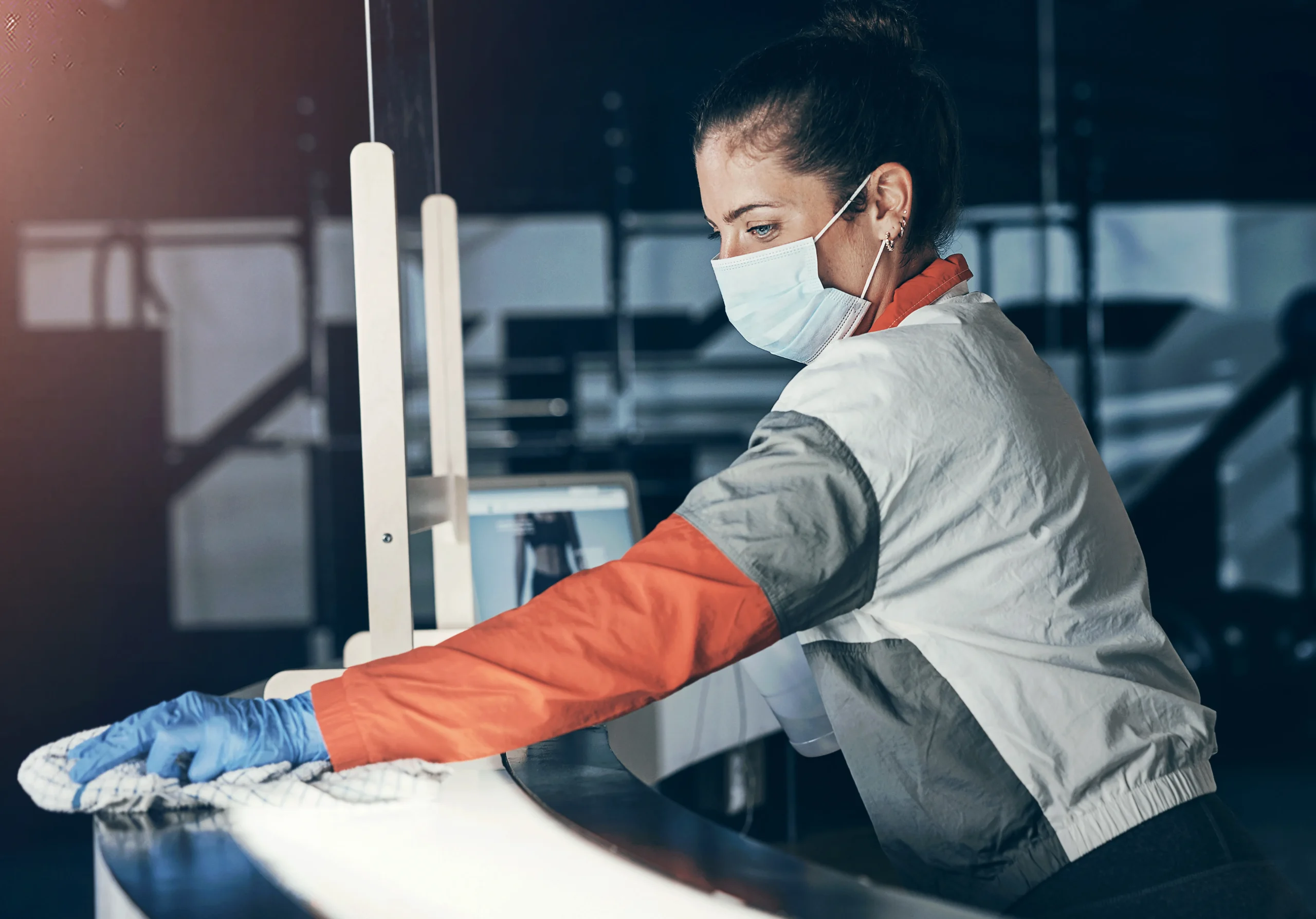 Fotografía de una mujer con cubrebocas y uniforme blanco con gris y naranja realizando servicio de limpieza industrial.