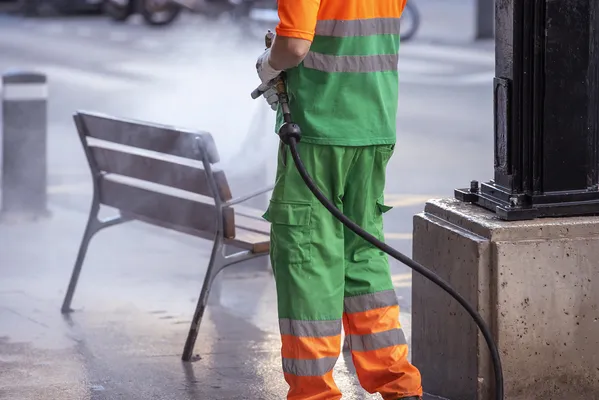 Fotografía de un operario de limpieza utilizando un uniforme color verde con naranja mientras realiza su trabajo.