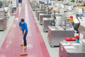 Servicio de limpieza para fábricas: Fotografía de un hombre de camisa azul rey barriendo el pasillo de una fábrica.